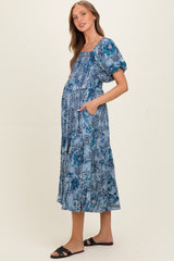 woman wearing a blue floral print maternity dress with puff sleeves and pockets, showcasing her baby bump