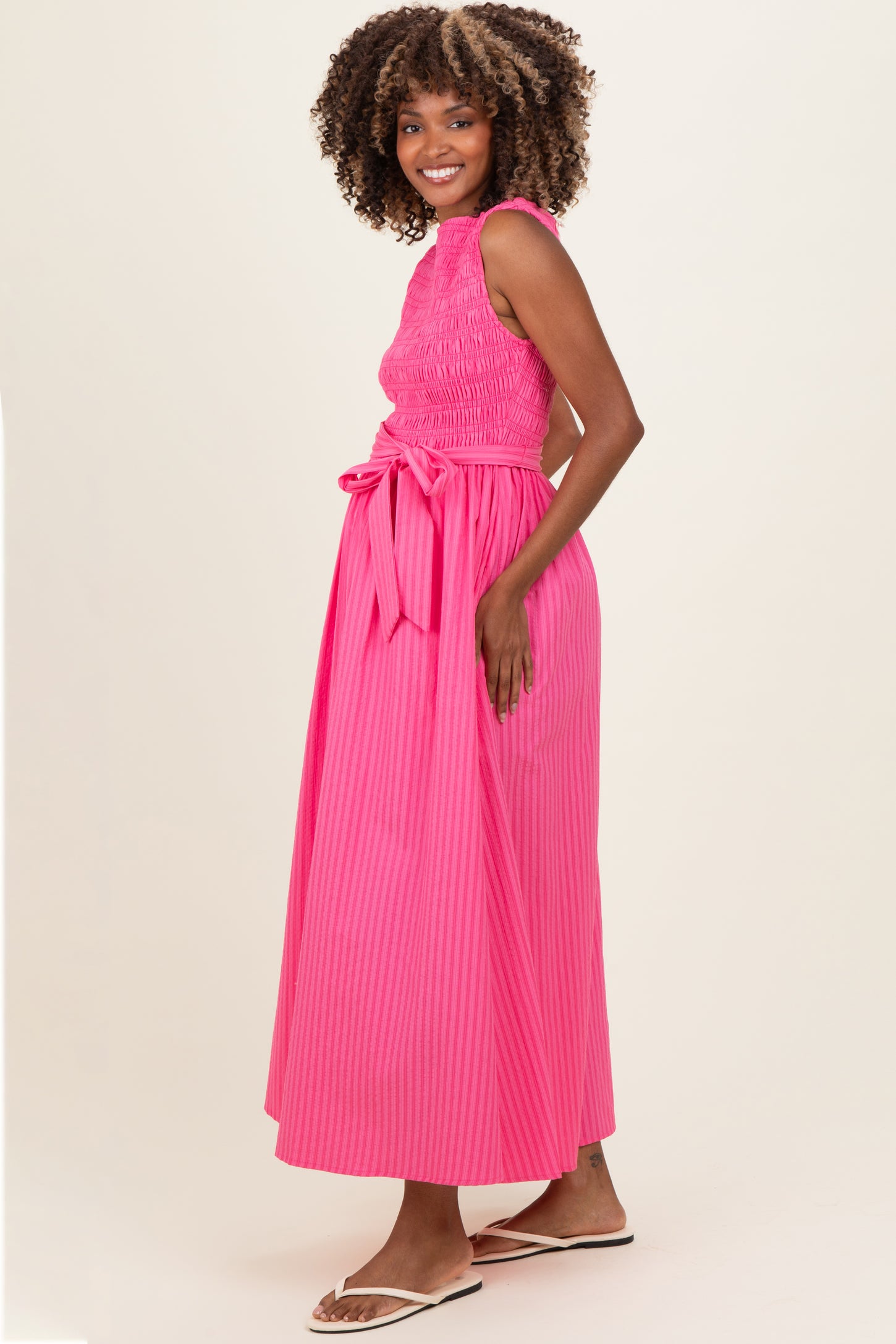 woman wearing a pink smocked maxi maternity dress with a tied waist and a visible baby bump