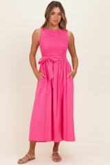 woman wearing a hot pink sleeveless dress with a smocked bodice and a tie waist, featuring side pockets