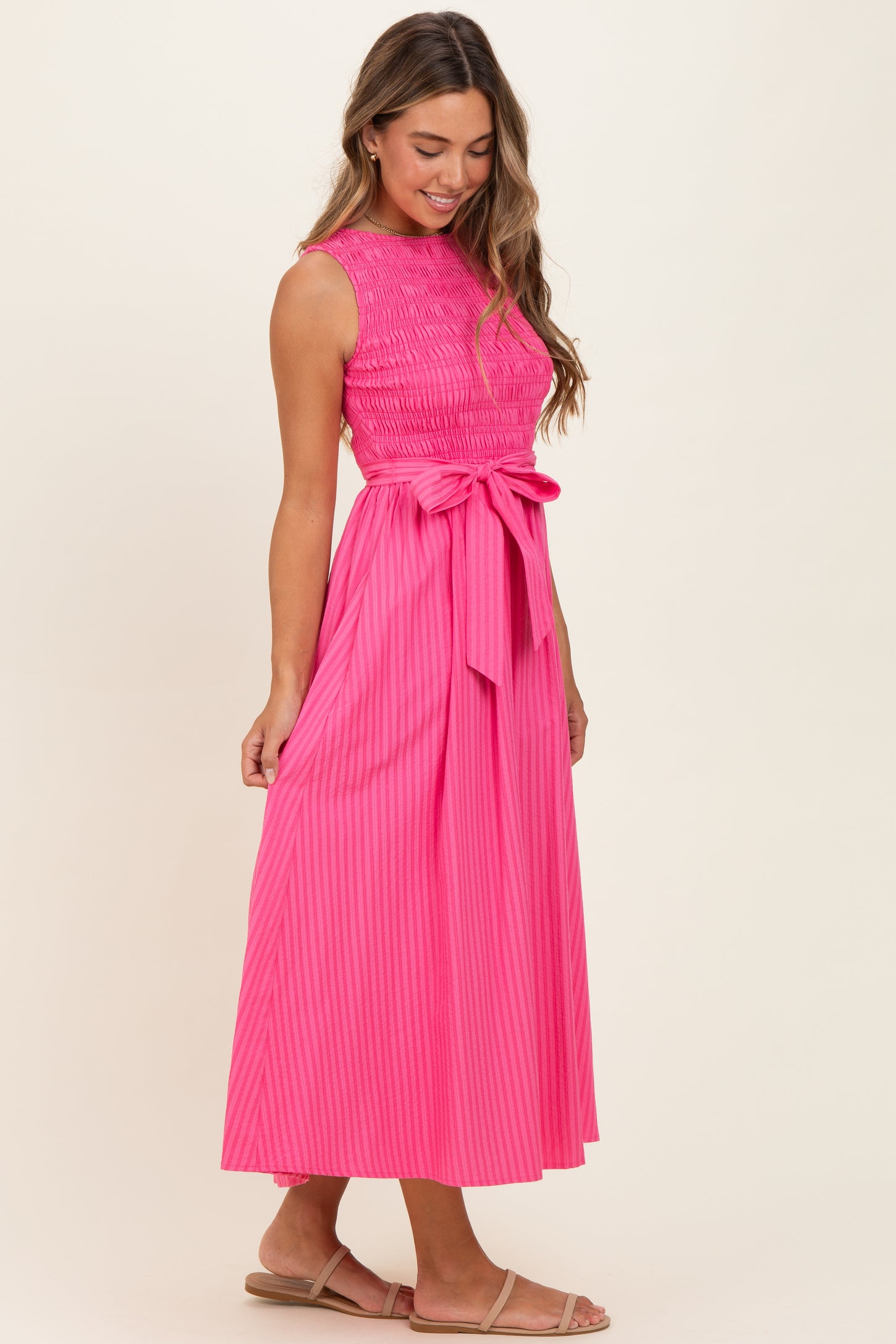 woman wearing a bright pink sleeveless maxi dress with a smocked bodice and a tie waist detail