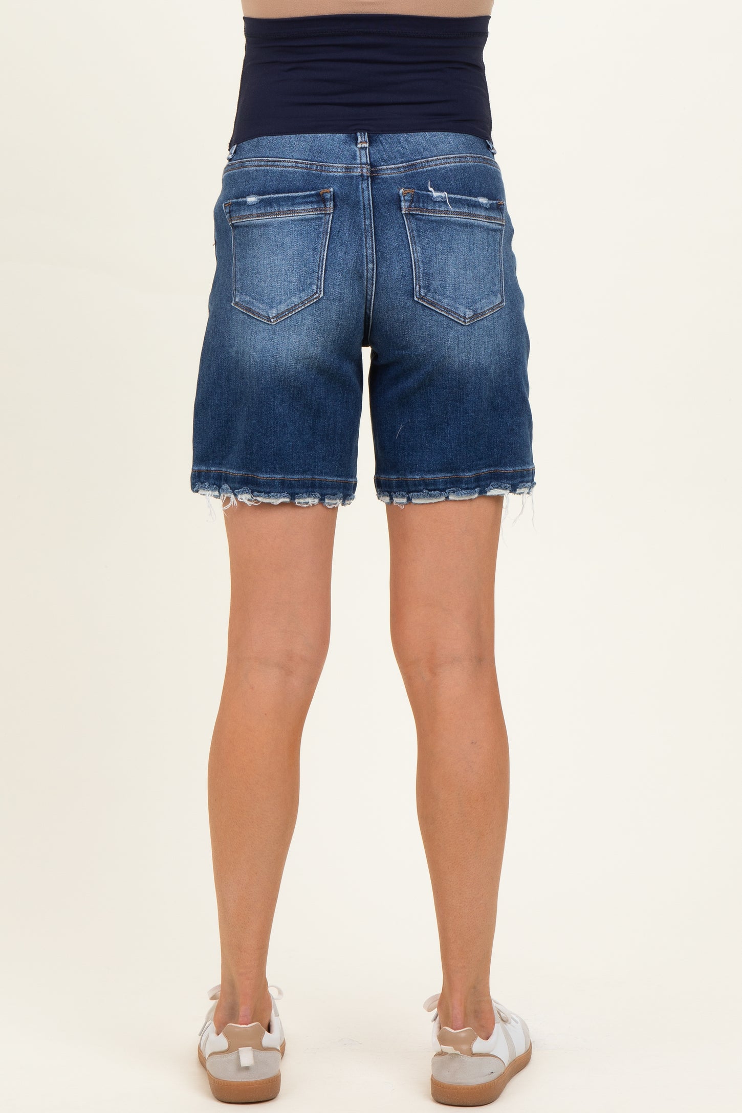 woman wearing a pair of dark blue denim maternity shorts, showing a frayed hem and back pockets