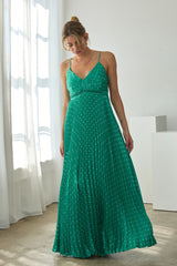 woman wearing a green pleated maxi dress with spaghetti straps and polka dot details, looking down at the floor