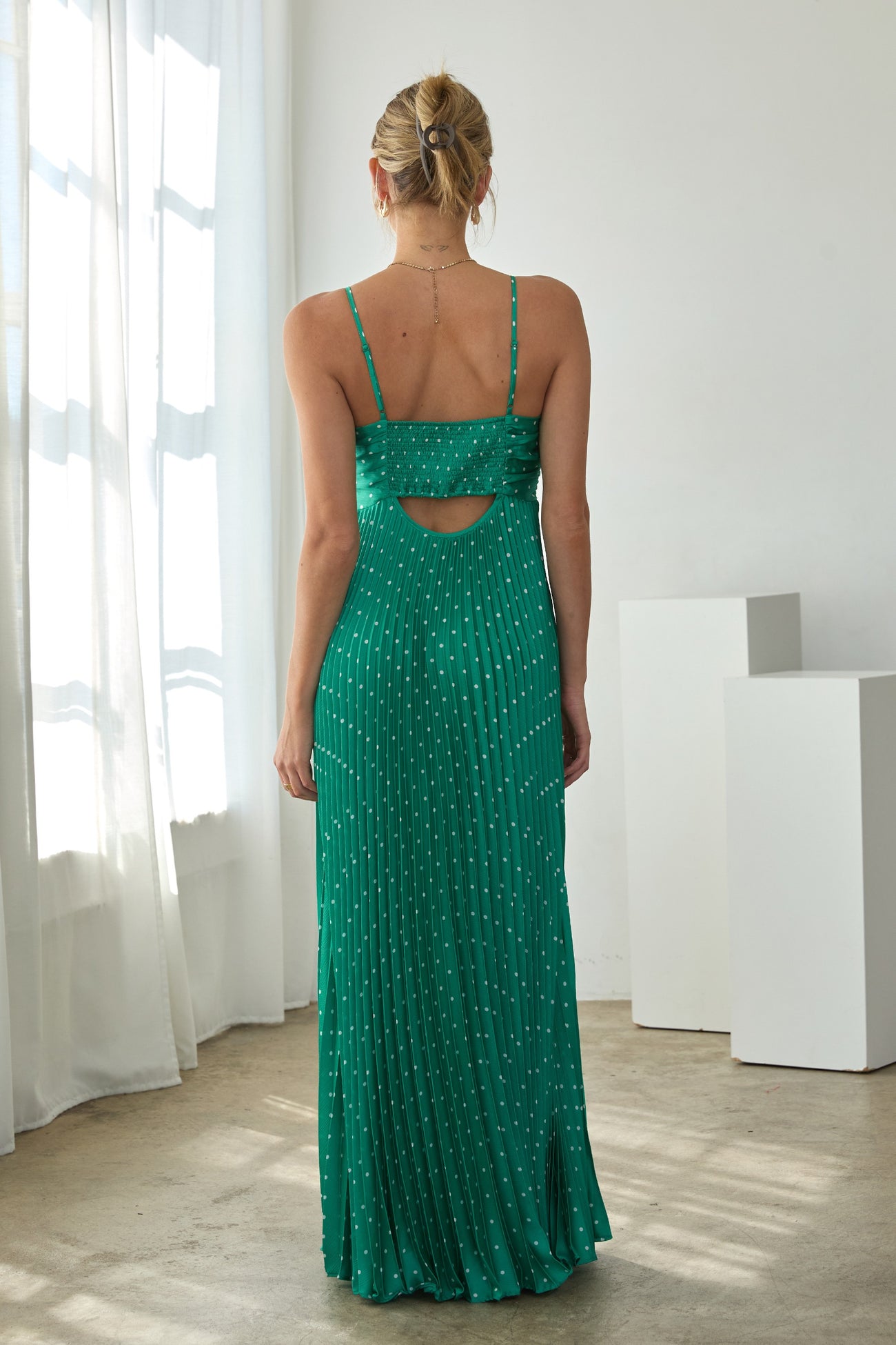 woman wearing a green spaghetti strap maxi dress with a cutout back and pleated design