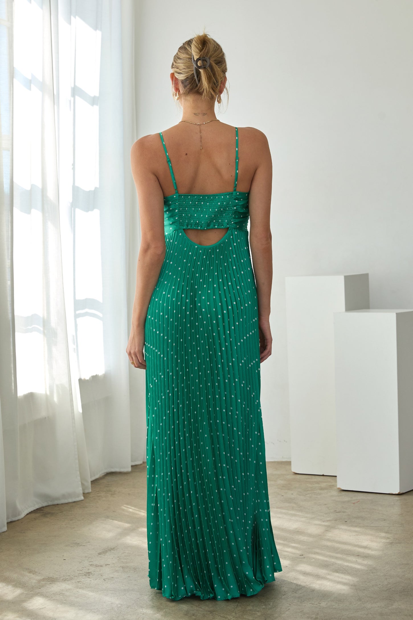 woman wearing a green spaghetti strap maxi dress with a cutout back and pleated design