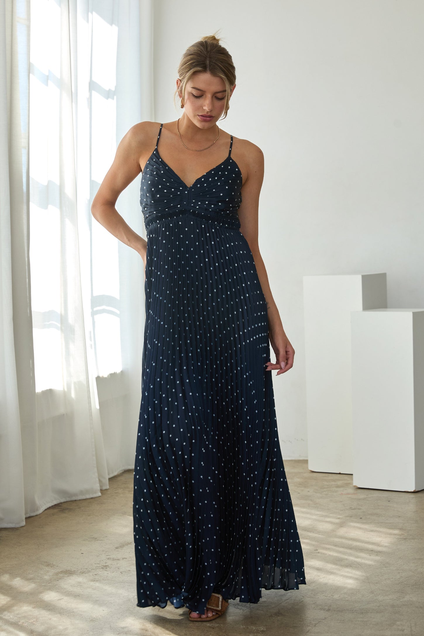 woman wearing a navy blue maxi dress with white polka dots and a fitted bodice, standing indoors in natural light