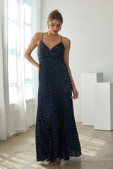 woman wearing a navy blue maxi dress with white polka dots and a fitted bodice, standing indoors in natural light