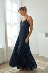 woman wearing a navy blue spaghetti strap maxi dress with white polka dots and a flowy skirt