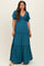 woman wearing a teal maternity maxi dress with puff sleeves and a smocked bodice, standing with a relaxed pose