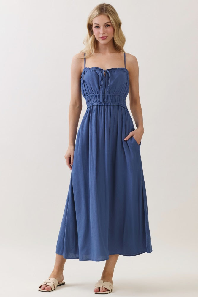woman wearing a blue maxi dress with adjustable straps and a drawstring waist, featuring pockets and a flowy silhouette