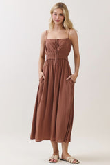 woman wearing a rust-colored maxi dress with spaghetti straps and pockets, smiling at the camera