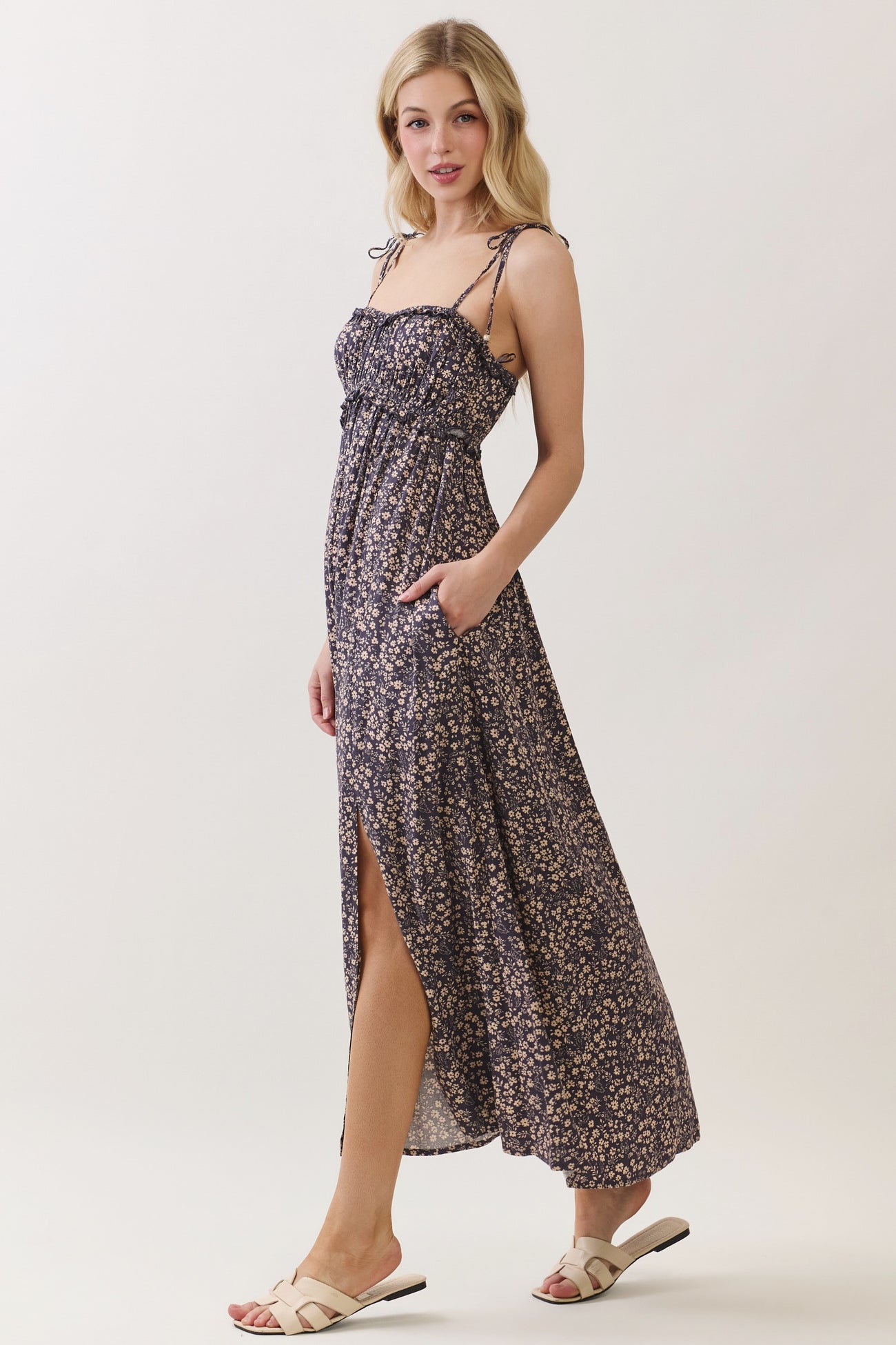 woman wearing a navy floral maxi dress with a cinched bodice, adjustable straps, and side pockets