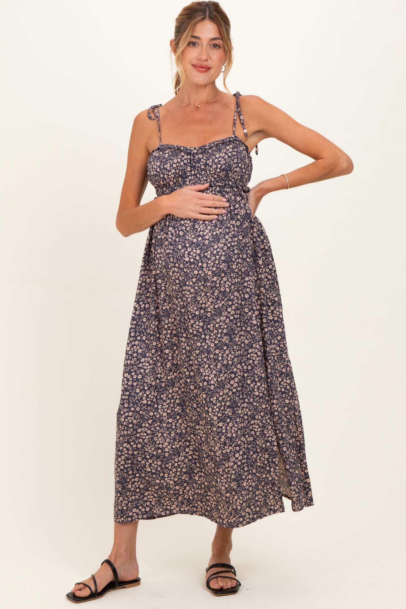 woman wearing a navy floral maternity maxi dress with tie straps and holding her baby bump