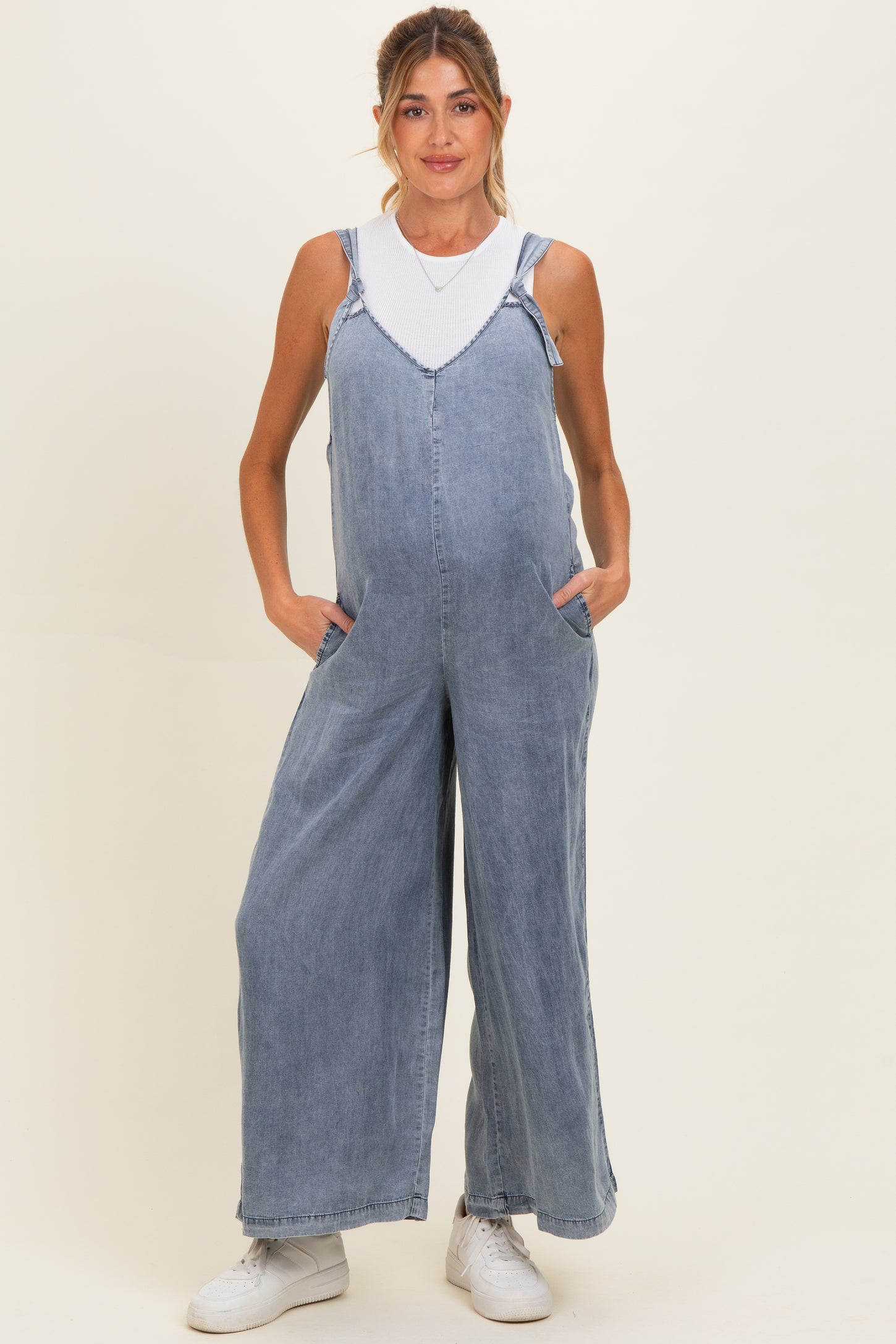 woman wearing a light wash denim maternity overall with wide legs and pockets, showcasing her baby bump