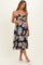 woman wearing a brown floral print maternity dress with adjustable straps and holding her baby bump