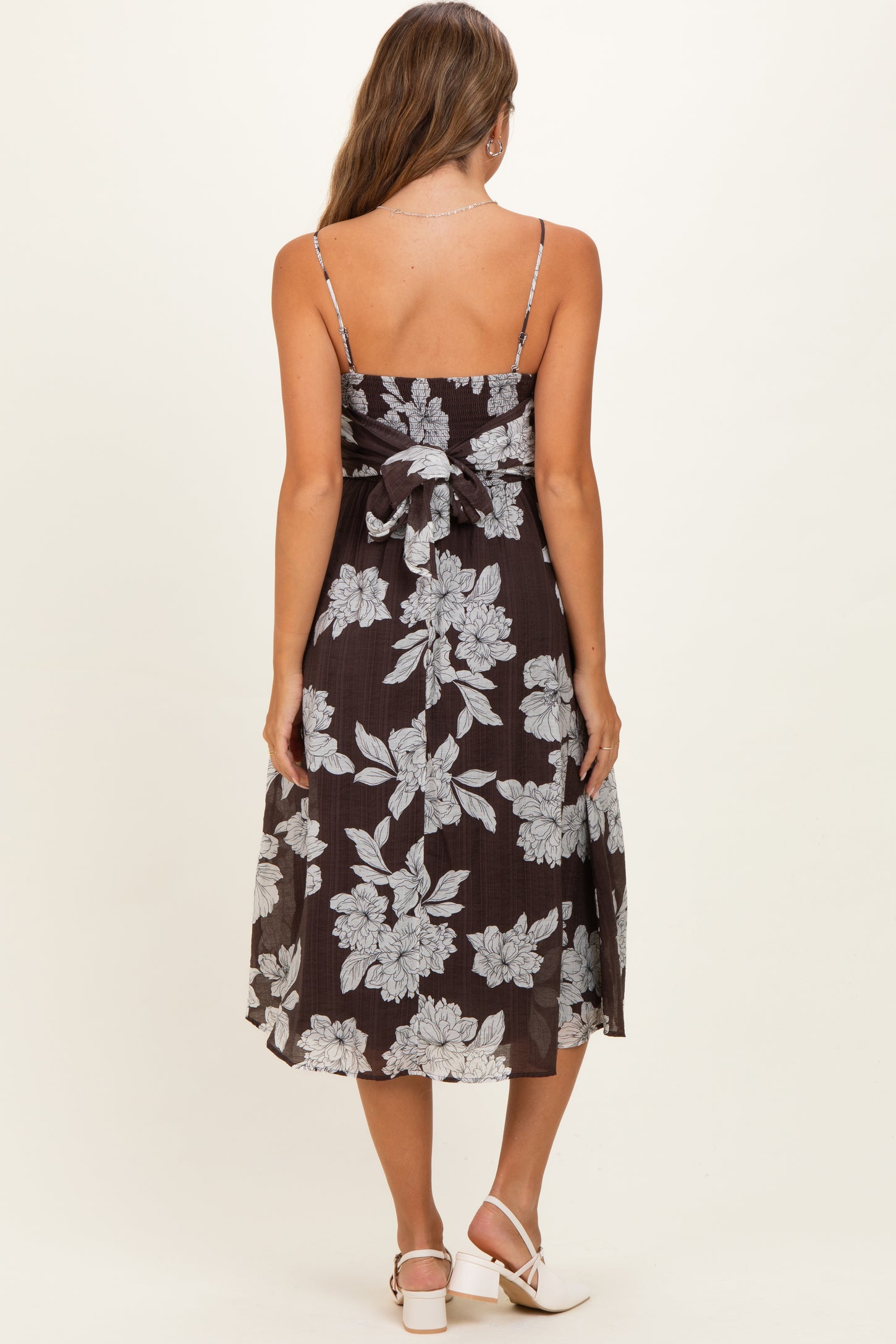 woman wearing a dark floral print maternity dress with thin straps and a bow detail at the back