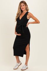 woman wearing a black sleeveless maternity dress with a tie waist and side slit, showcasing her baby bump