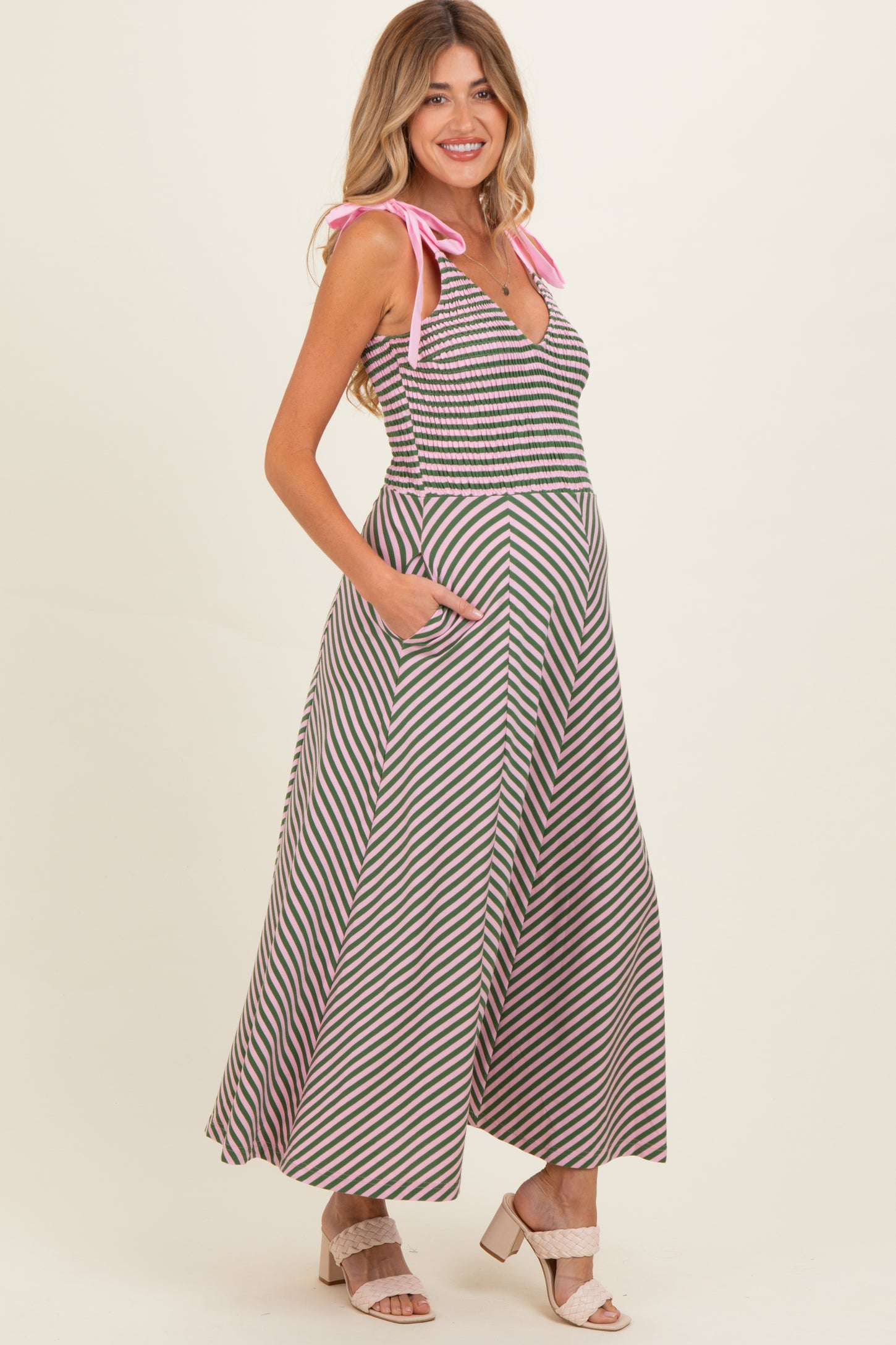 woman wearing a striped maternity maxi dress with pink tie straps and pockets, showing her baby bump