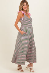 woman wearing a striped maternity maxi dress with pink tie straps and pockets, showing her baby bump