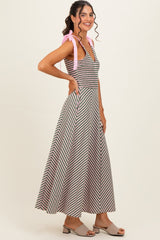 woman wearing a striped maxi dress with pink tied straps and a fitted bodice, smiling and standing sideways