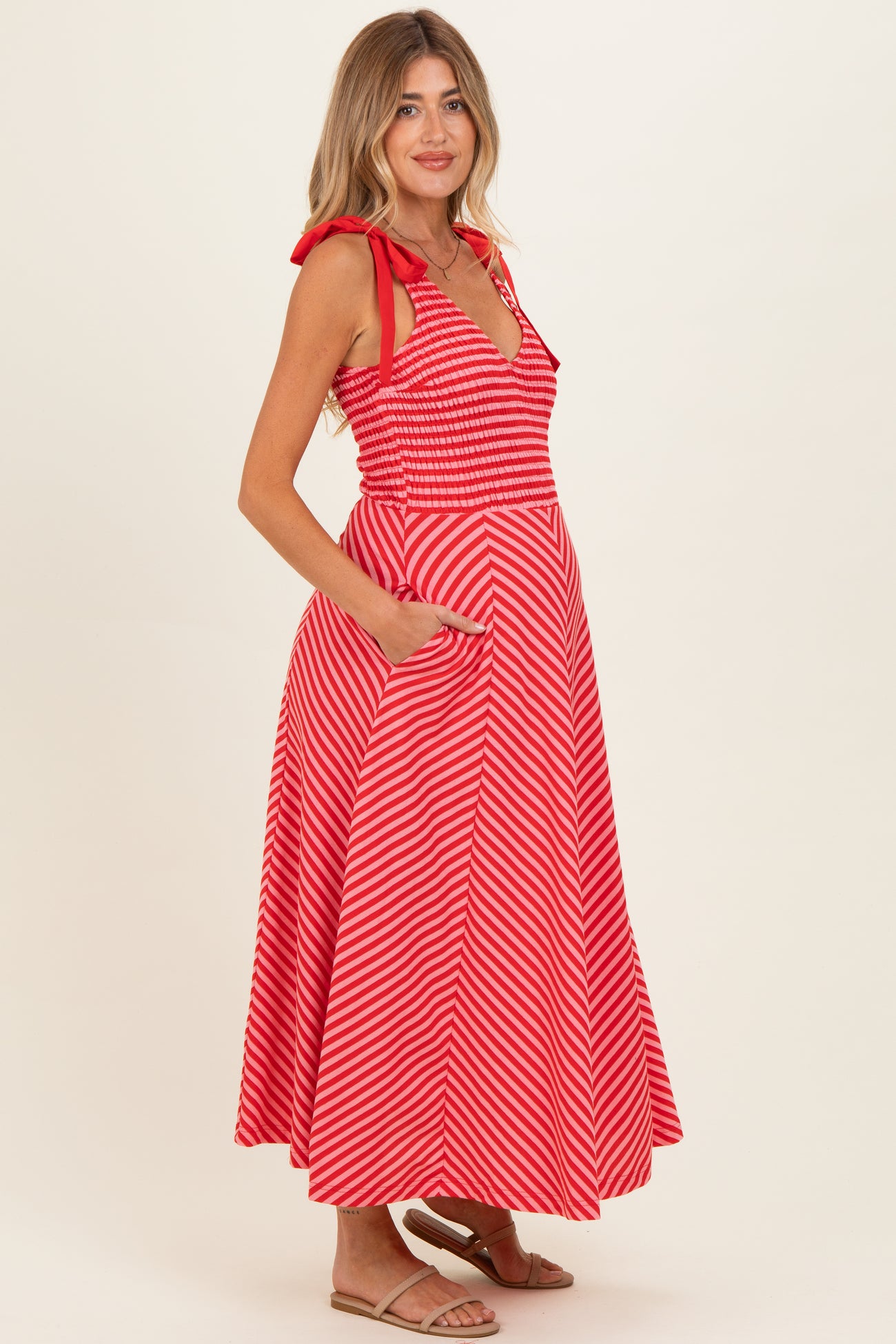 woman wearing a red and white striped maternity dress with a smocked bodice and pockets, showcasing her baby bump