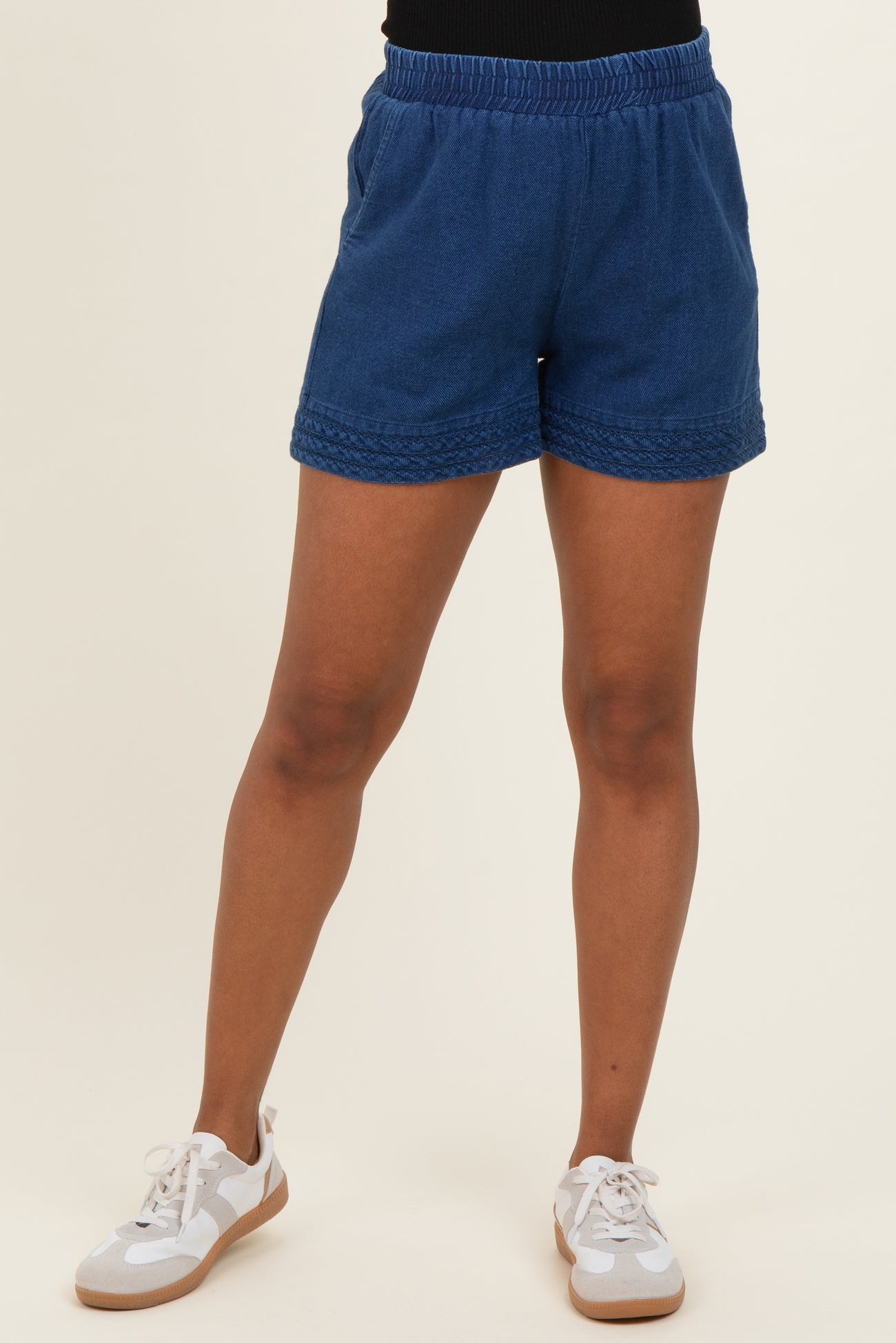 woman wearing navy blue maternity shorts with an elastic waistband and braided detail, styled with white sneakers