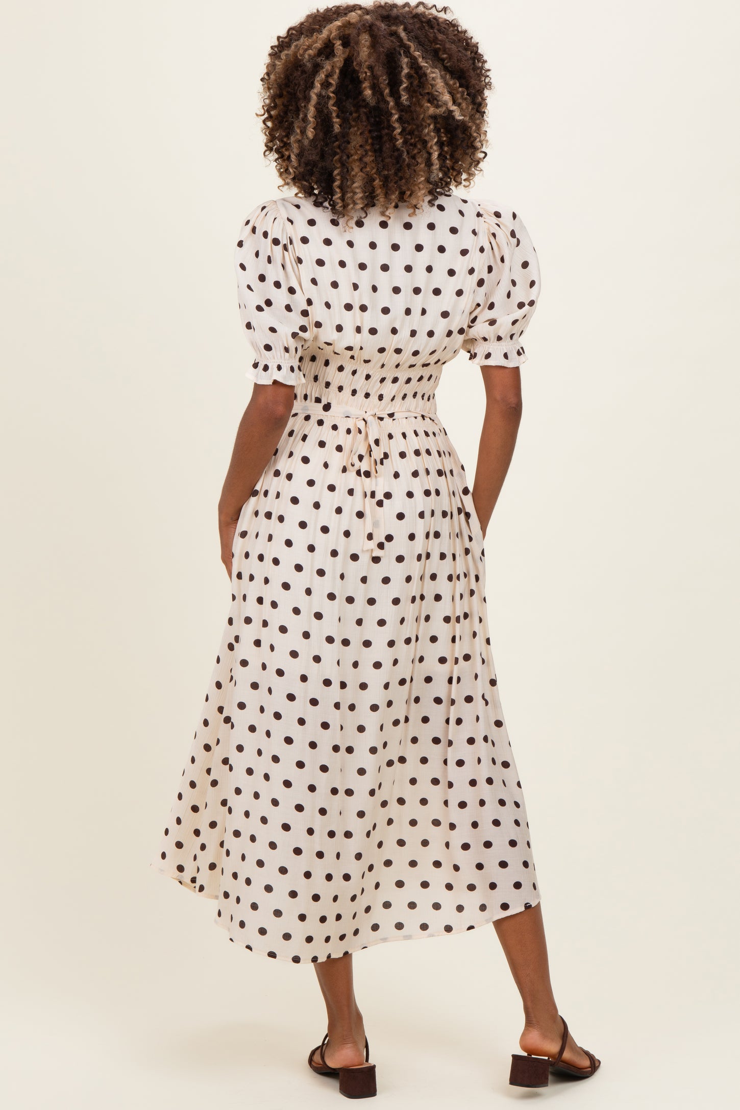 woman wearing a cream maternity dress with brown polka dots and puff sleeves, showing the back view