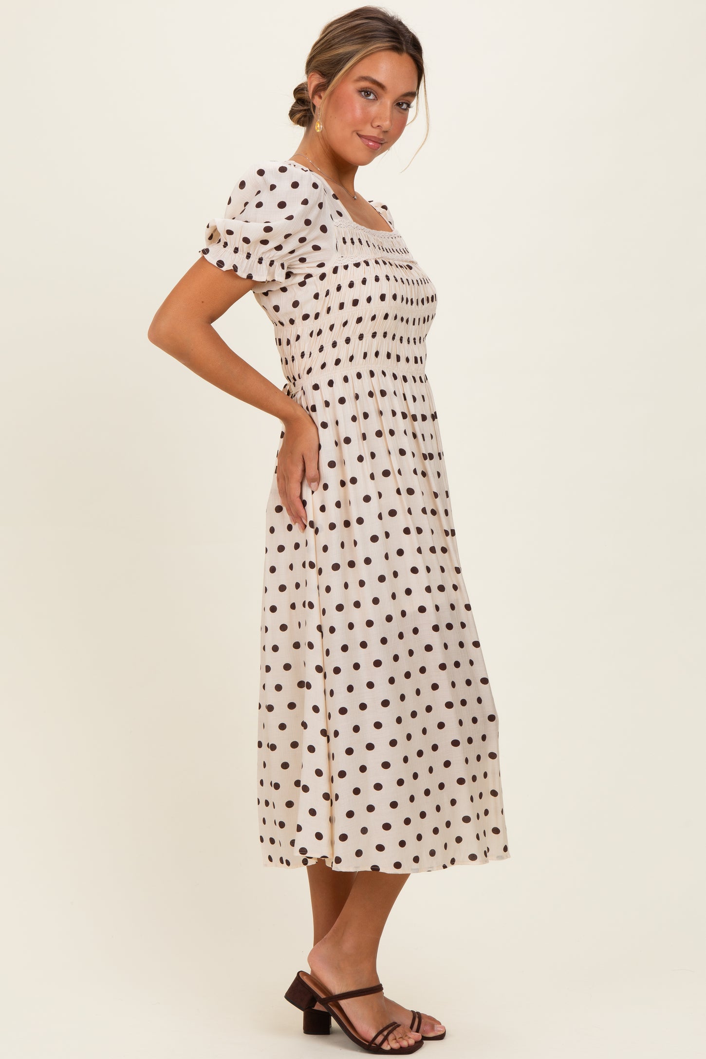 woman wearing a cream-colored midi dress with black polka dots and puff sleeves, standing in profile