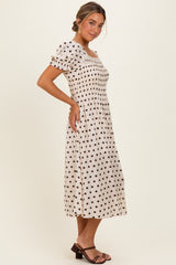 woman wearing a cream-colored midi dress with black polka dots and puff sleeves, standing in profile