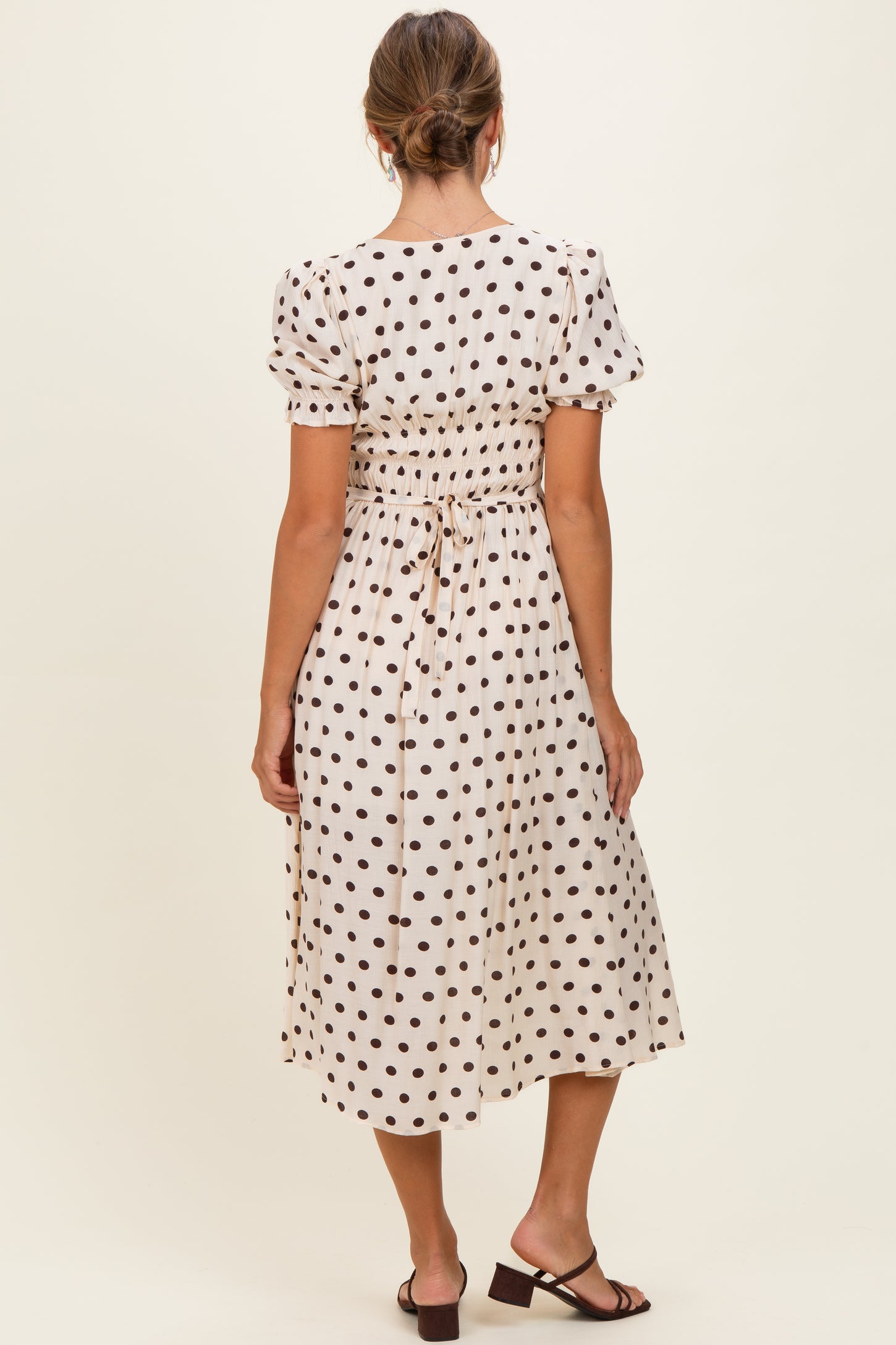 woman wearing a cream polka dot midi dress with short puff sleeves and a cinched waist, viewed from the back