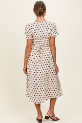 woman wearing a cream polka dot midi dress with short puff sleeves and a cinched waist, viewed from the back