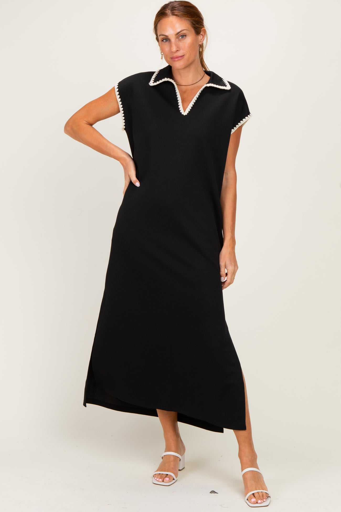 woman wearing a black maxi dress with a white collar and side slit, standing with one hand on her hip