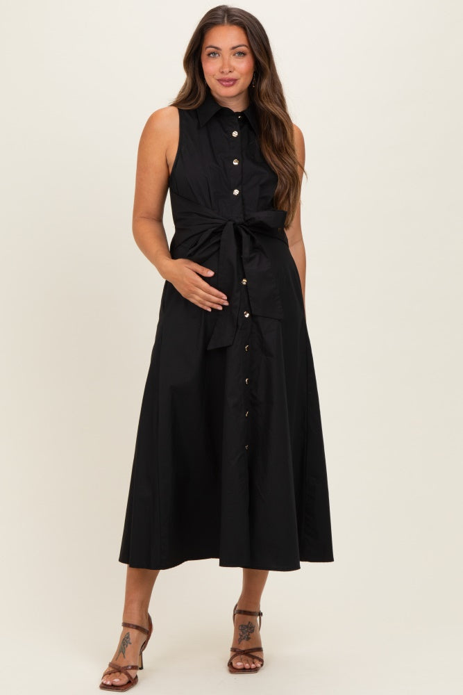 woman wearing a black sleeveless maternity dress with a tie around the waist and button details, holding her baby bump