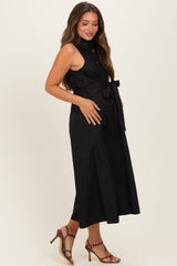 woman wearing a black sleeveless maternity dress with a tie waist and a visible baby bump