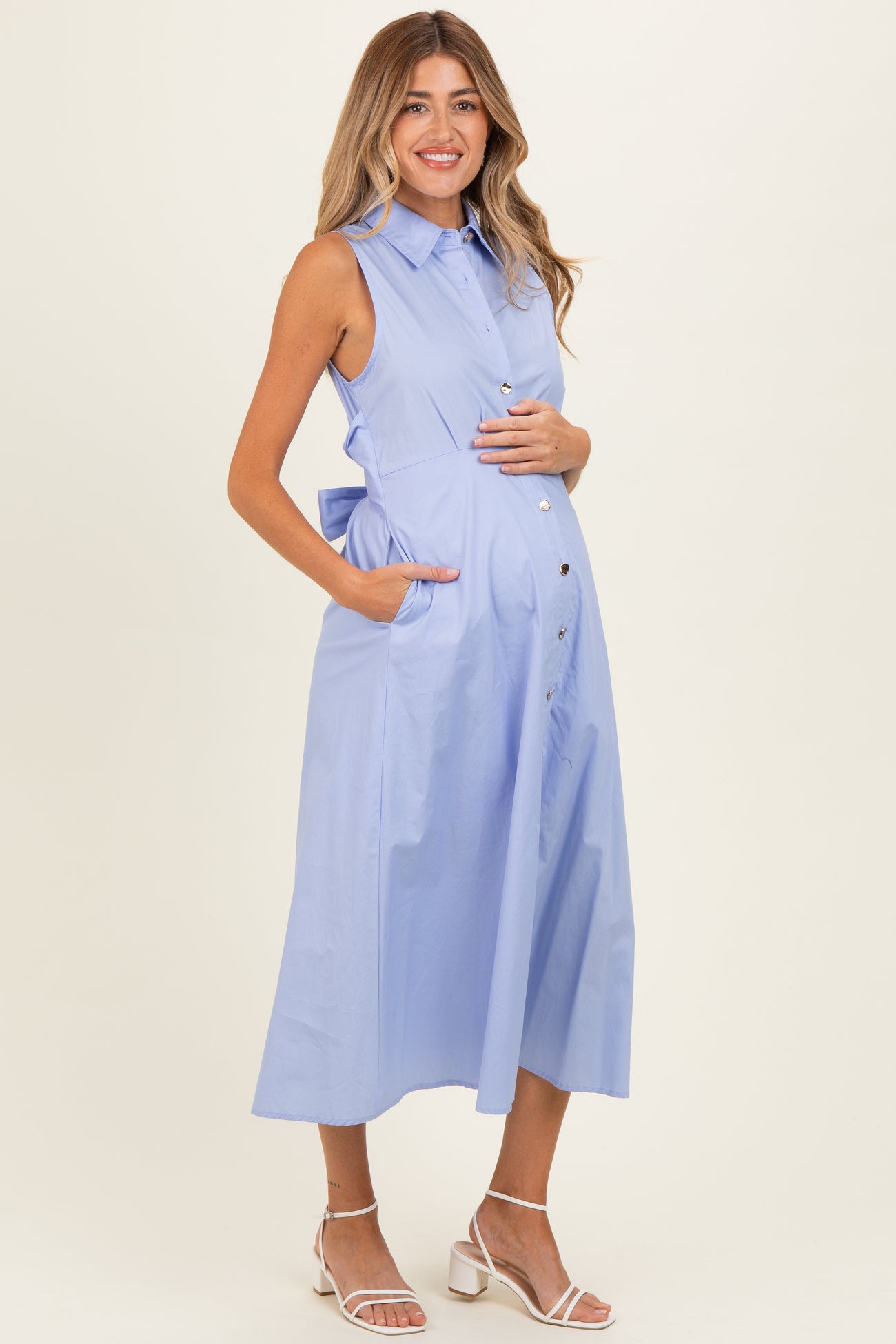 woman wearing a light blue sleeveless maternity dress with a button-down front and pockets, showing her baby bump