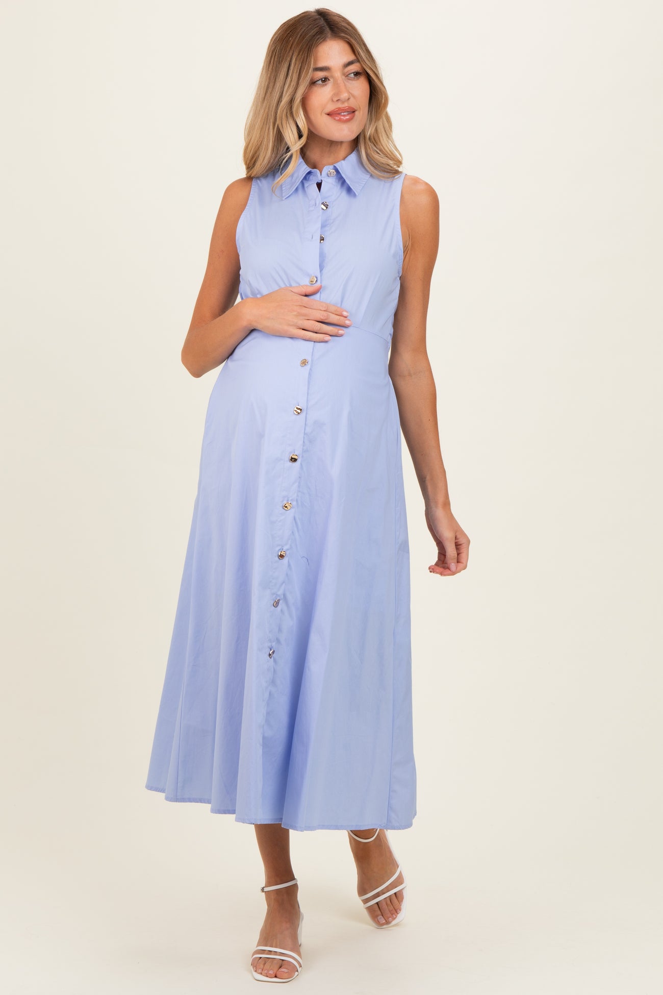 woman wearing a light blue sleeveless maternity dress with button details and holding her baby bump