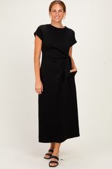 woman wearing a black short sleeve maxi dress with a tied waist and pockets, smiling at the camera