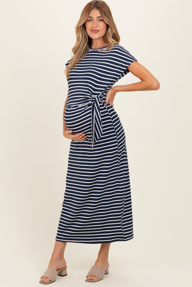 woman wearing a navy and white striped maternity maxi dress with a tie detail and holding her baby bump