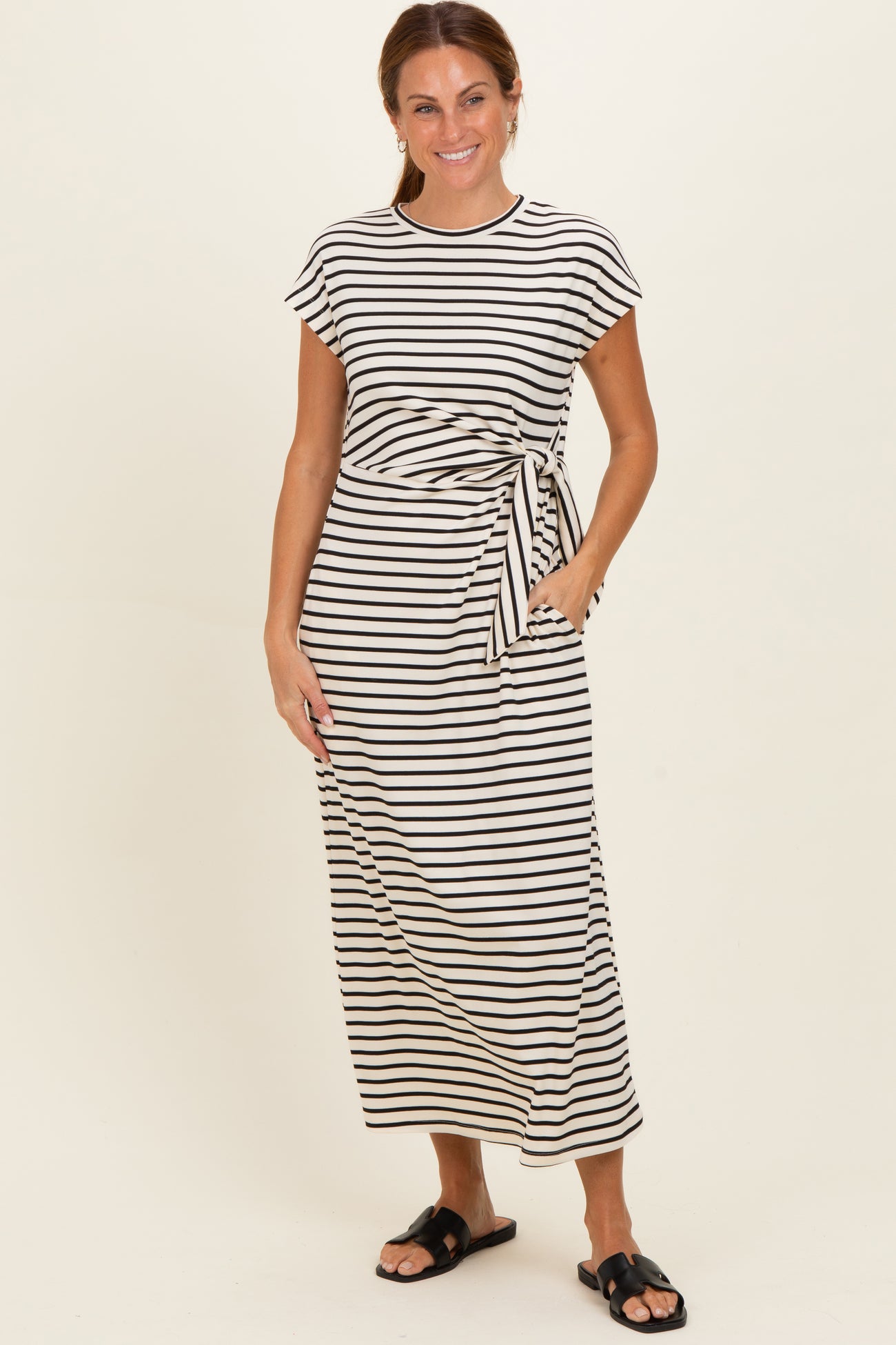 woman wearing a striped maxi dress with short sleeves and a side tie, posed with hands in pockets