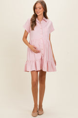 woman wearing a pink button-up maternity dress with short sleeves and a tiered ruffle hem, showing her baby bump