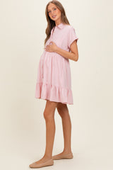 woman wearing a light pink maternity dress with short sleeves and a ruffled hem, holding her baby bump
