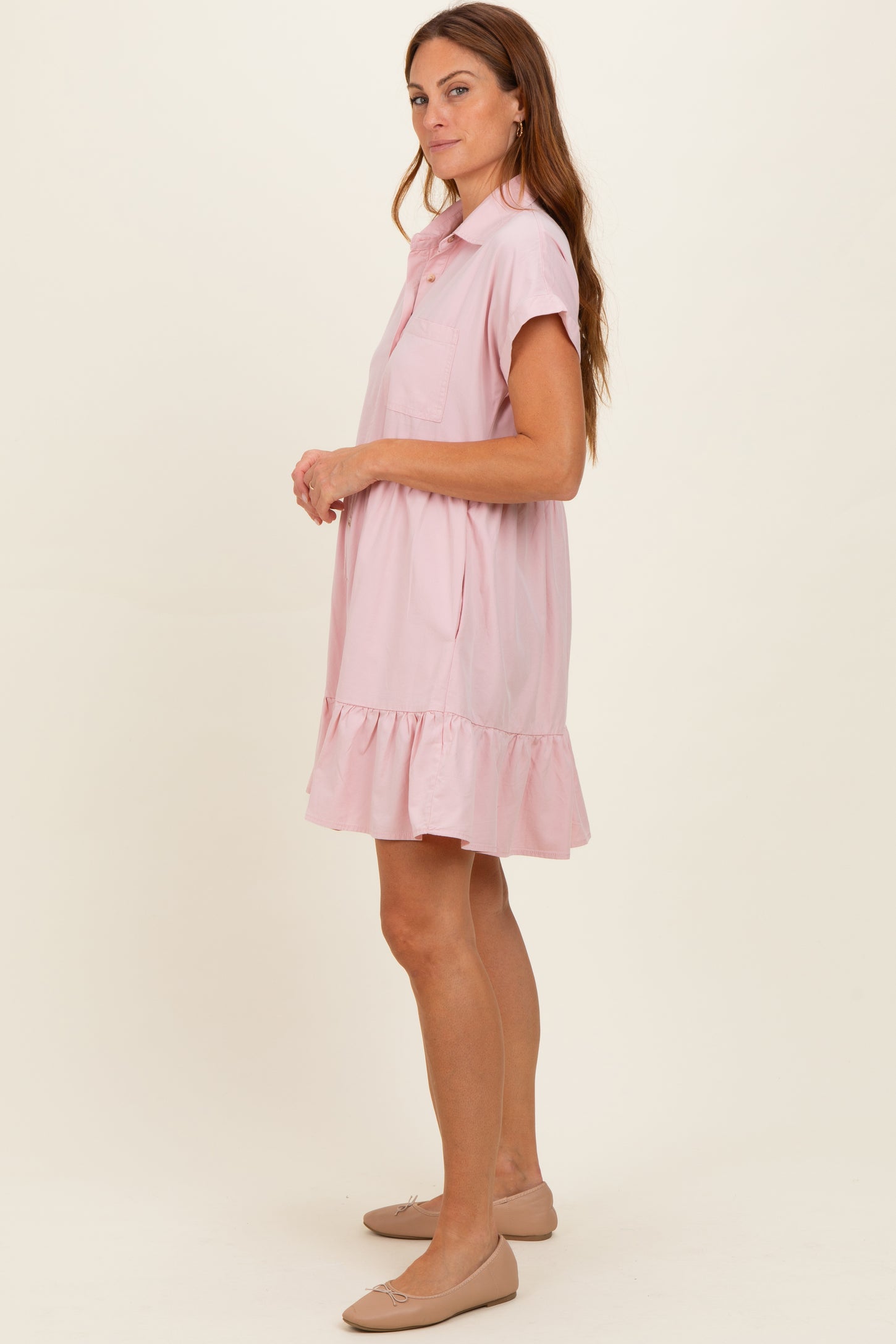woman wearing a light pink short sleeve shirt dress with a ruffled hem and a pocket on the chest