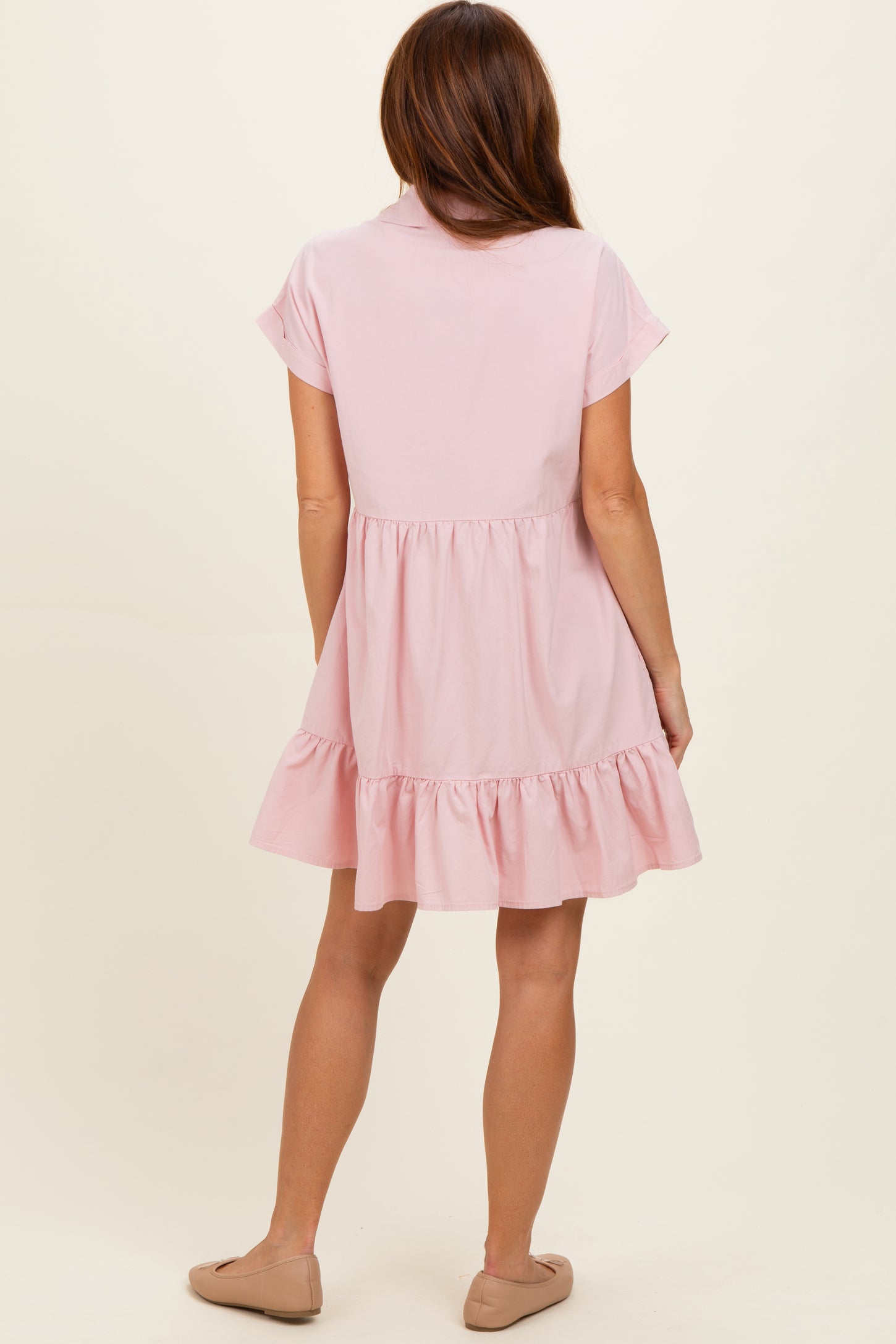 woman wearing a light pink short sleeve dress with a tiered ruffle hem and a collared neckline, viewed from the back
