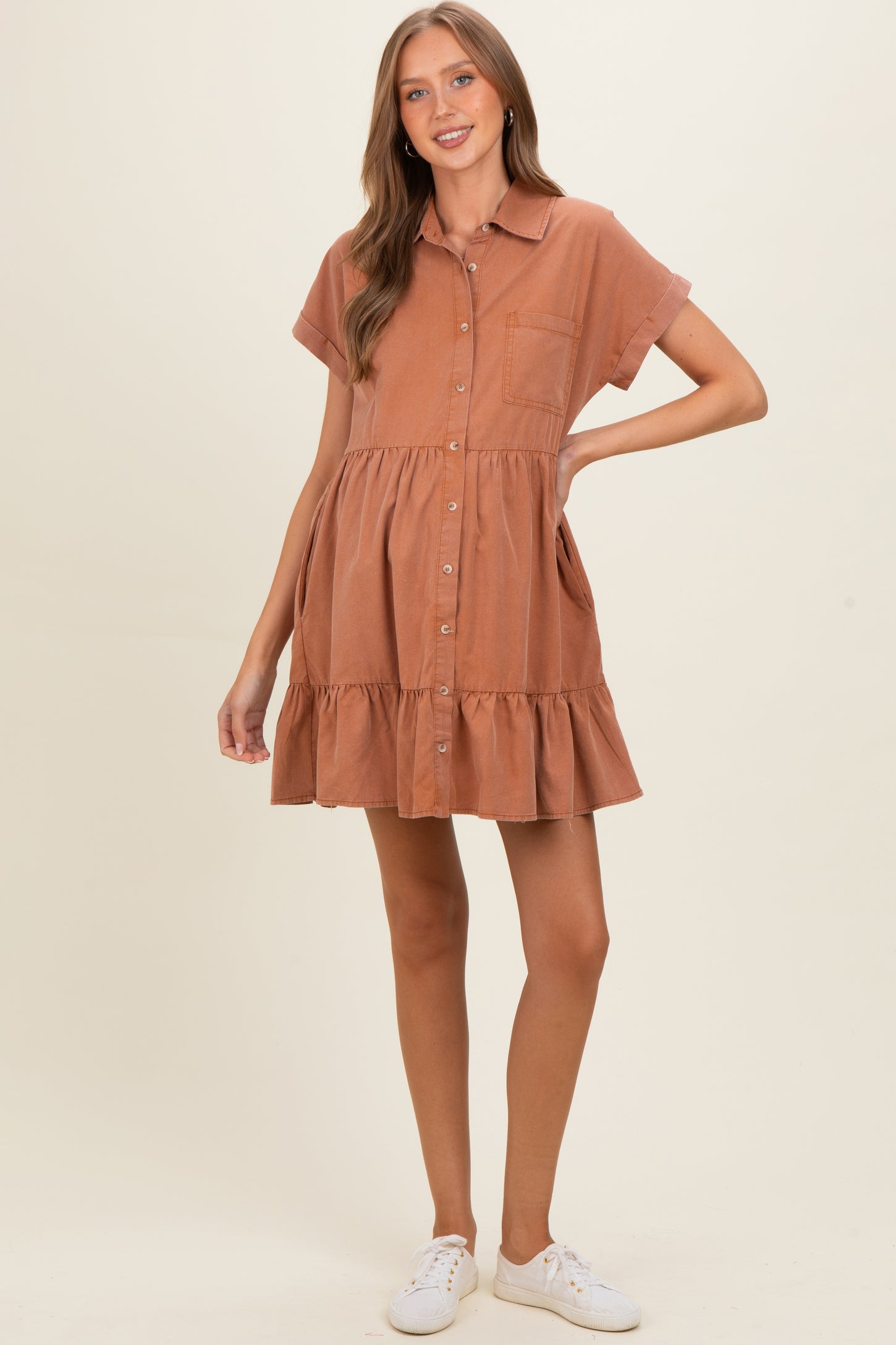 woman wearing a rust-colored short sleeve maternity dress with a button front and ruffle hem