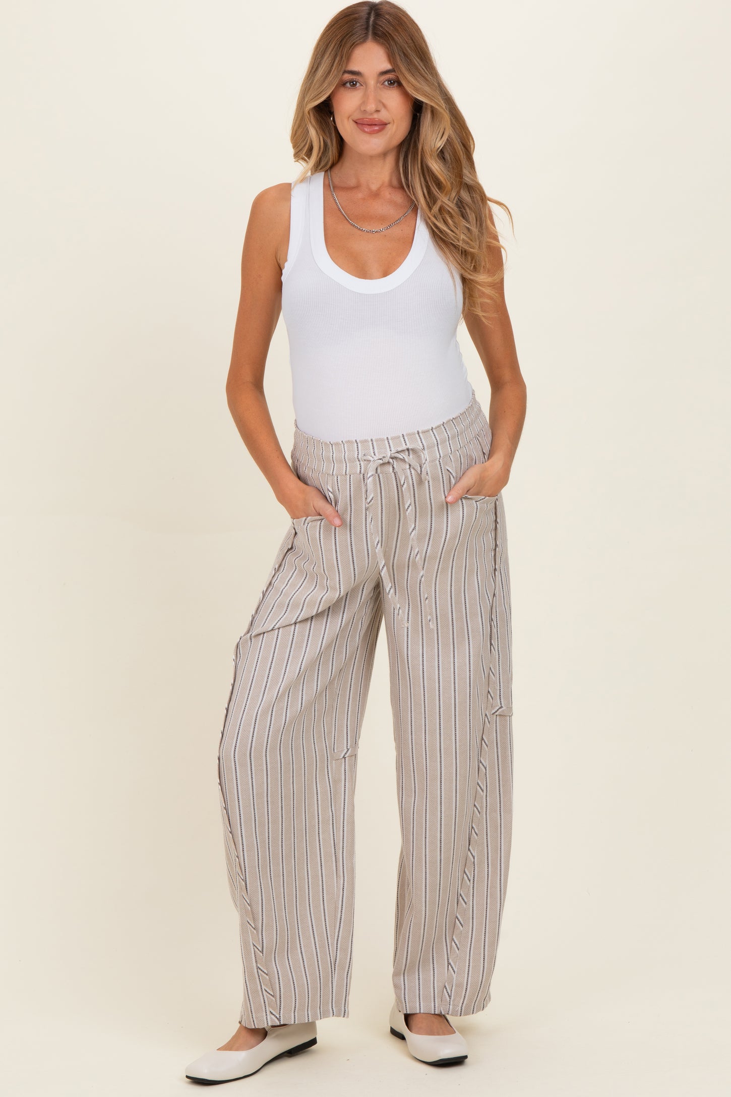 woman wearing a white tank top and light striped maternity pants with pockets, standing casually