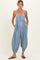 woman wearing a light blue maternity jumpsuit with a v-neckline, button details, and pockets, holding her baby bump