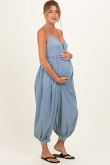 woman wearing a light blue maternity jumpsuit with button details and holding her baby bump
