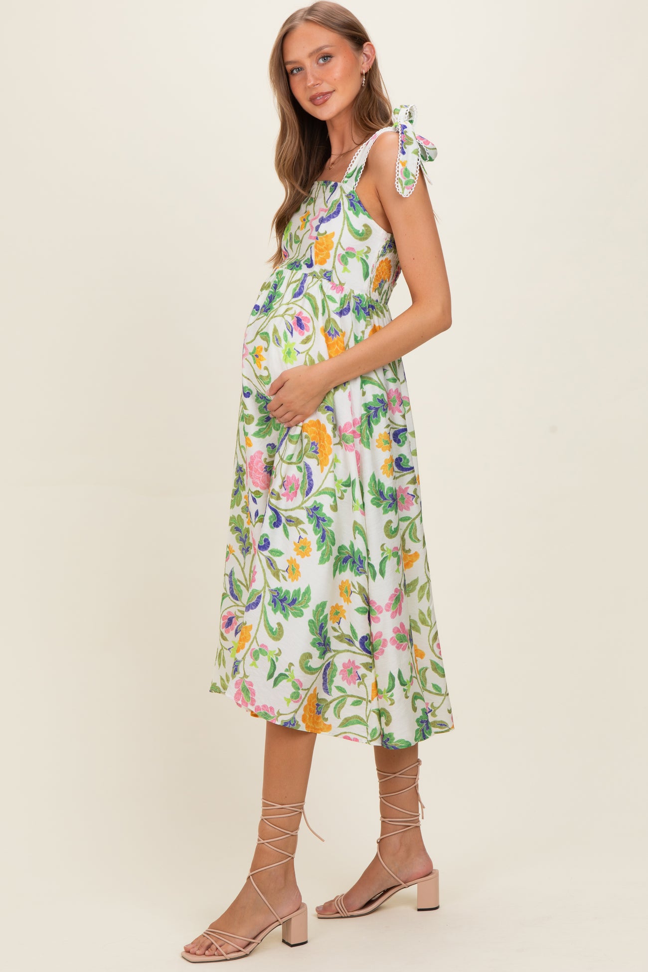 woman wearing a floral print maternity dress with tie straps and holding her baby bump