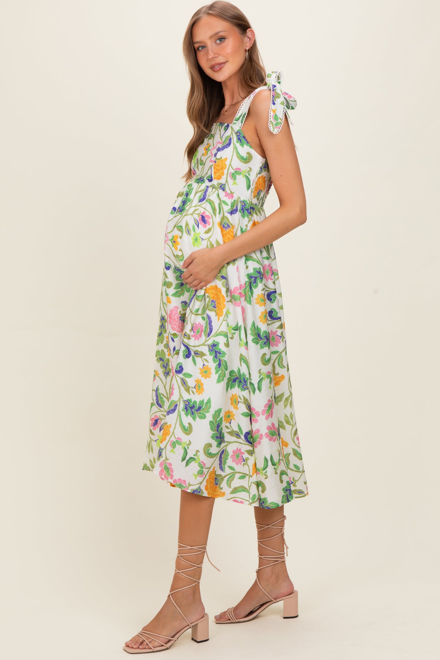 woman wearing a floral print maternity dress with tie straps and holding her baby bump