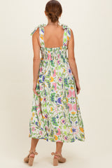 woman wearing a floral maxi dress with tie straps and smocked back, showcasing a vibrant green pattern with colorful flowers