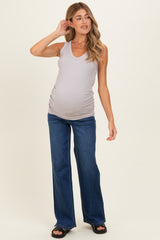 woman wearing a light gray maternity tank top and blue flared maternity jeans, showcasing her baby bump
